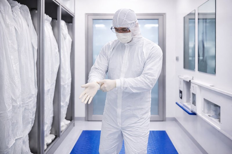 Cleanroom technician in full PPE carefully putting on gloves while standing on a tacky mat in a controlled gowning area before entering a clean room environment.