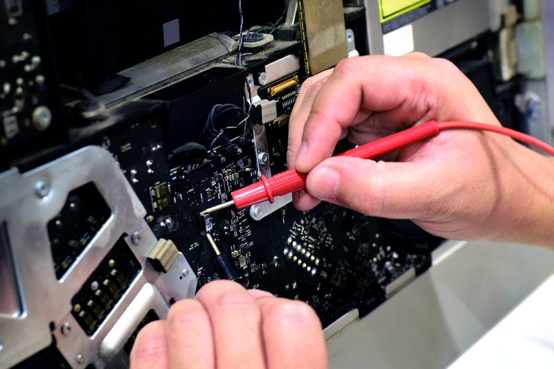 A technician uses a red multimeter probe to carefully diagnose and repair the intricate internal components of a damaged server.