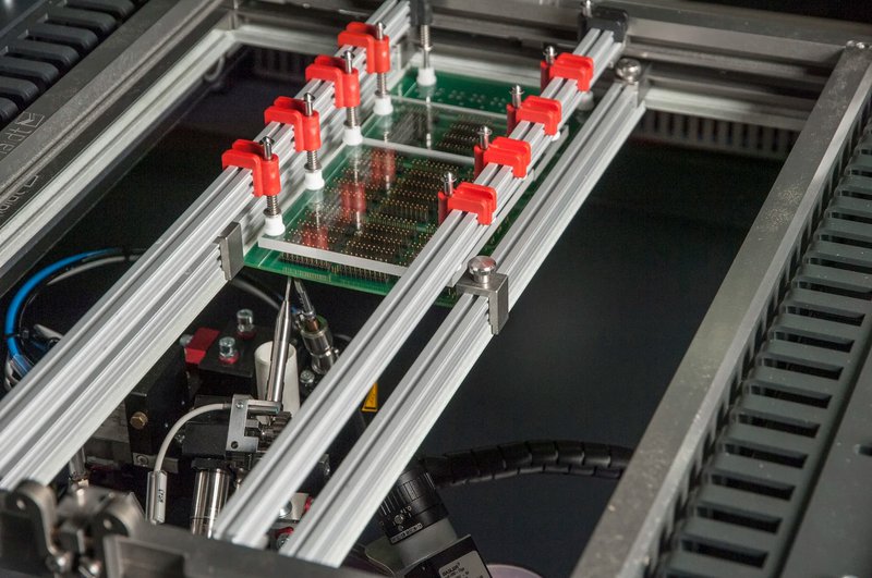 This photo features a PCB being processed in a soldering machine