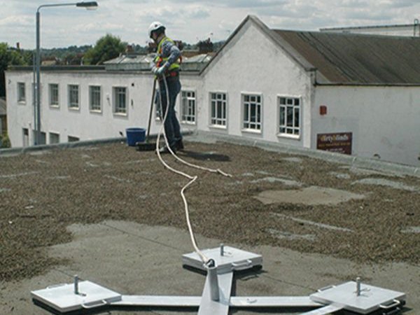 A worker using one of the many roof anchors for fall protection by Safety Rail Source