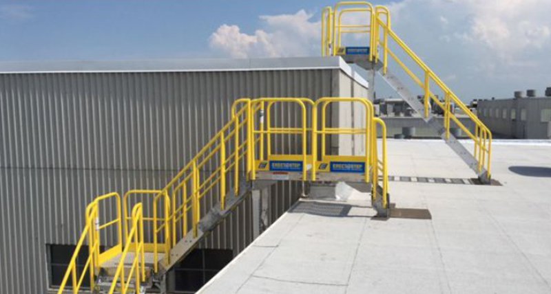 Yellow aluminum railing for stairs on ErectaStep crossover stairways connecting two rooftop levels at an industrial facility