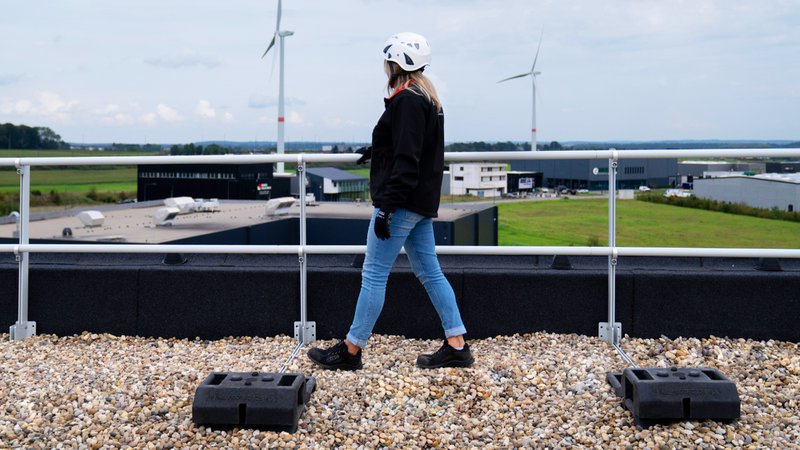 A worker walks beside rooftop railing for construction projects that need permanent fall protection