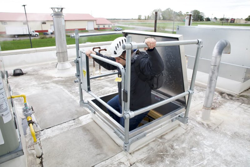 The image shows a person going up a Roof Hatch Lift & Lock. The person is wearing a black jacket and white helmet.