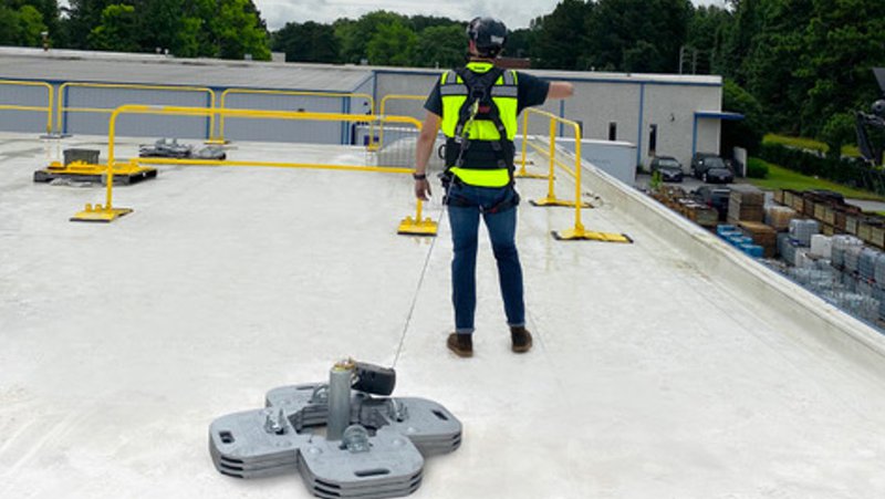 Worker tied off to a horizontal lifeline system anchor point on a flat commercial rooftop with guardrails in the background