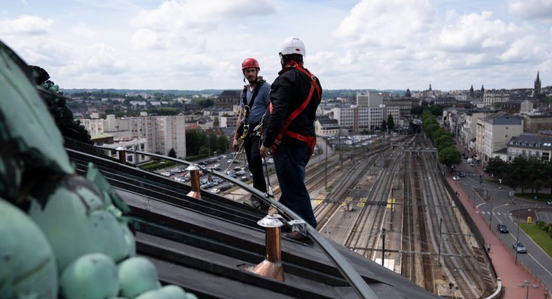 Two workers connected to a horizontal lifeline system on a slanted rooftop at height