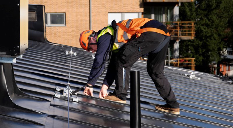 Worker in safety harness inspecting a metal roof in compliance with OSHA roofing standards