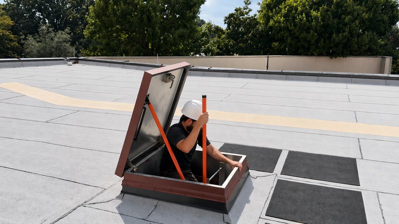 Worker uses roof hatch access point on a flat rooftop