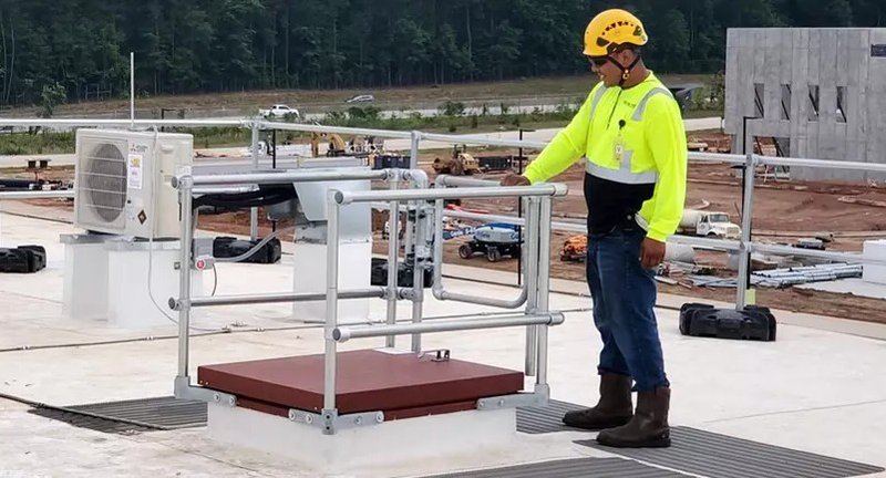 A maintenance personnel wearing a hard hat conducting a roof assessment. He's right beside a roof hatch that's compliant with OSHA regulations.