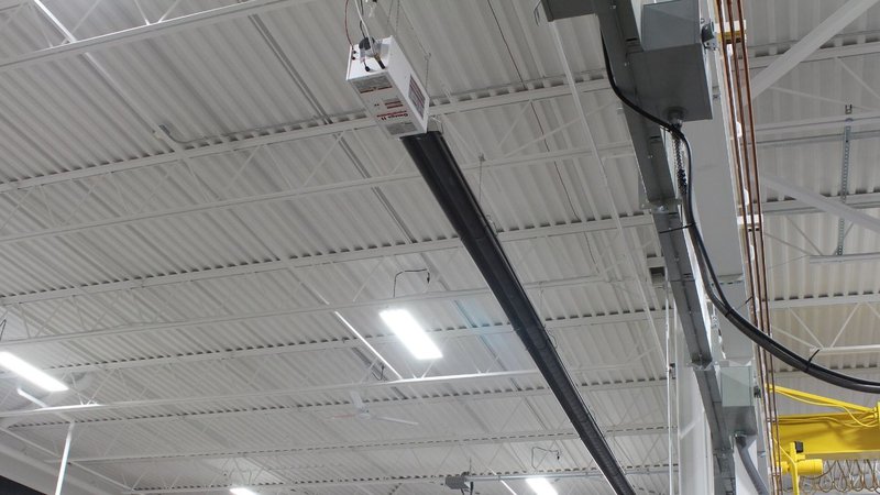 A commercial infrared tube heater for shop environments mounted to a warehouse ceiling.
