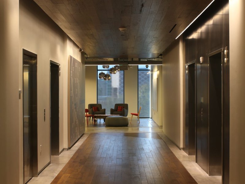 An elevator lobby that uses wood ceilings through vertically placed planks. Wood flooring is also used to complement the aesthetic