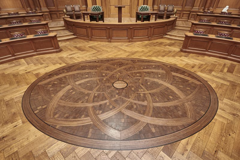 The image shows a handcrafted medallion designed by Woodwright as part of their professional hardwood floor installation for the Old Parkland Campus in Dallas, Texas.