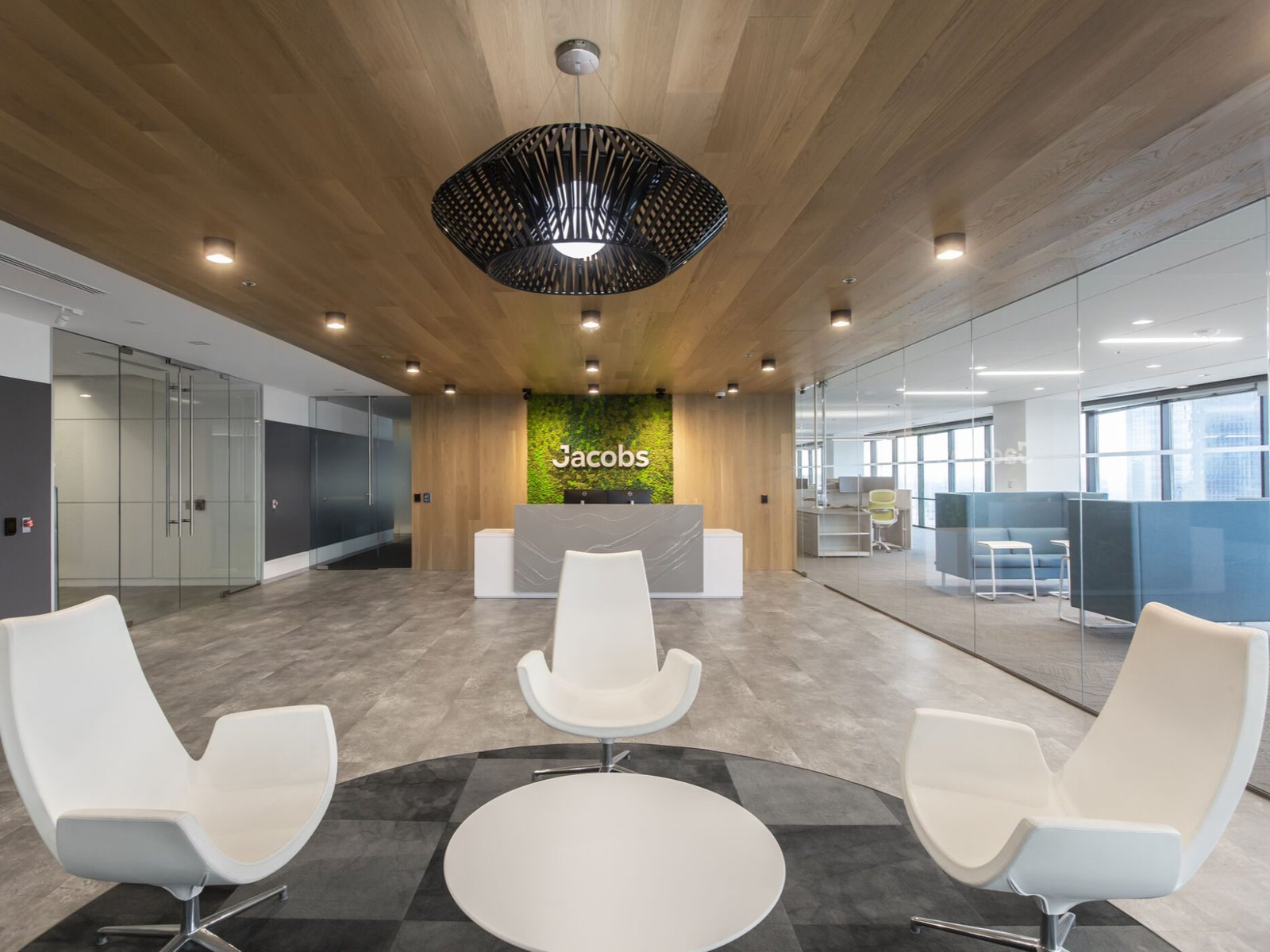The image shows the use of European Oak in a corporate office. The image shows three chairs, a circular table, and a logo of Jacobs