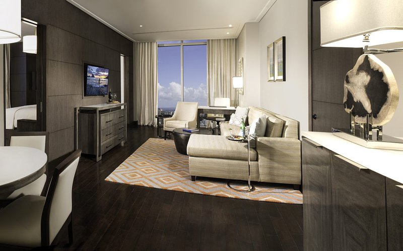 The image shows a hotel room that uses Texas Mesquite wood flooring and is adorned by furnitures such as a couch, cabinets, a chair, and others. 