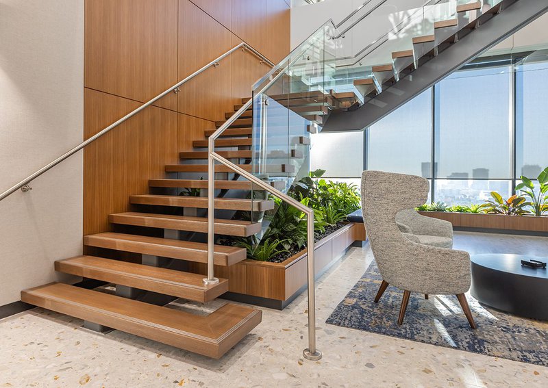 The image shows modern stairs at M Financials installed by Woodwright. Select Rift White Oak is used for the box treads and the outside part of the stairs is adorned with glass.
