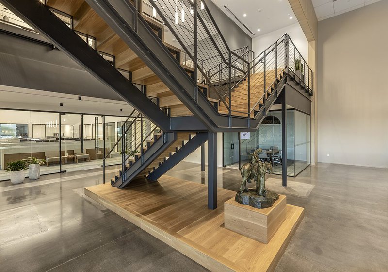 An image showing wood stair treads as the focal point of the photo. A horse statue, glass office, and and a big office space can be seen in the foreground and background.
