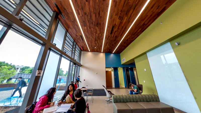 The image shows three people talking to one another as they discuss their notes. A wood plank ceiling is prominently shown in the image, which provides a contrast to the light colors of the interior.