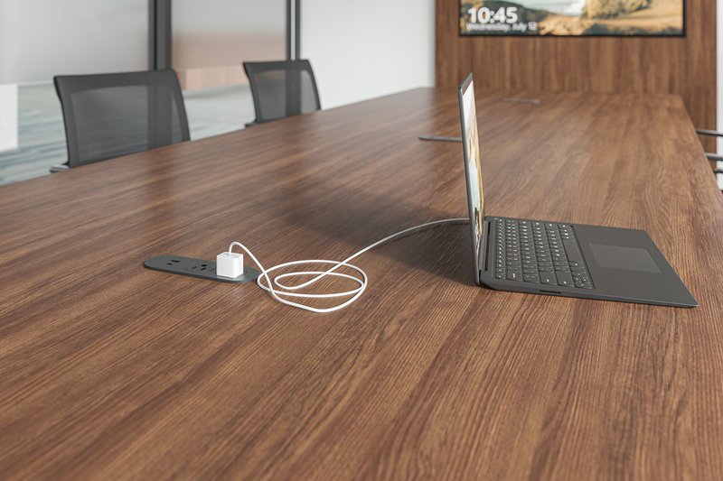 The image shows a recessed outlet that's integrated to a conference table. The outlet is being used to charge a laptop.