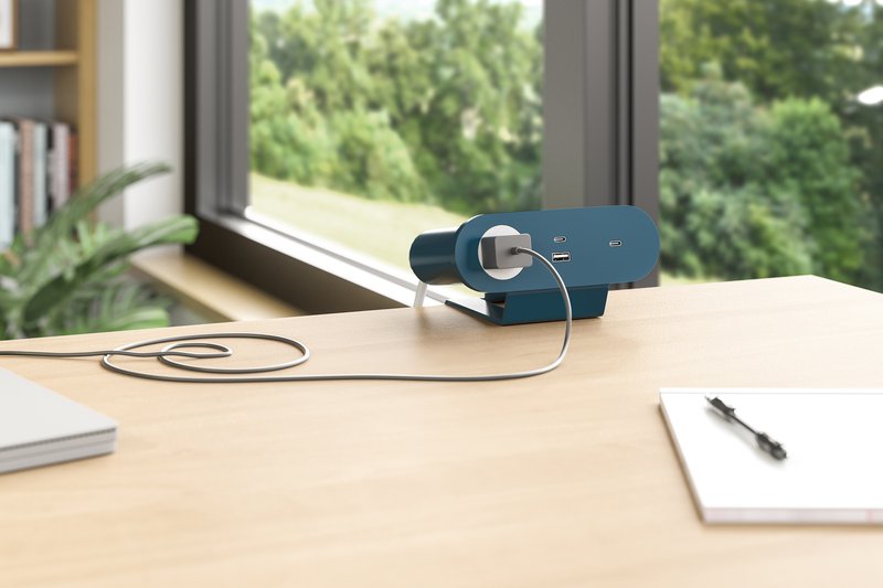 The image shows a power module mounted on top of a desk. A small charging brick is currently hooked to the outlet, presumably to charge a laptop.