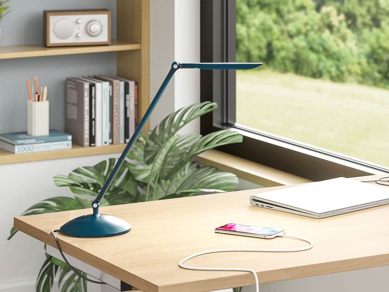 The image shows a workstation using a single arm desk light from LightCorp. The workstation is situated near a window.