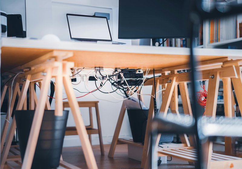 This photo features an office desk and power distribution unit with cluttered cable management