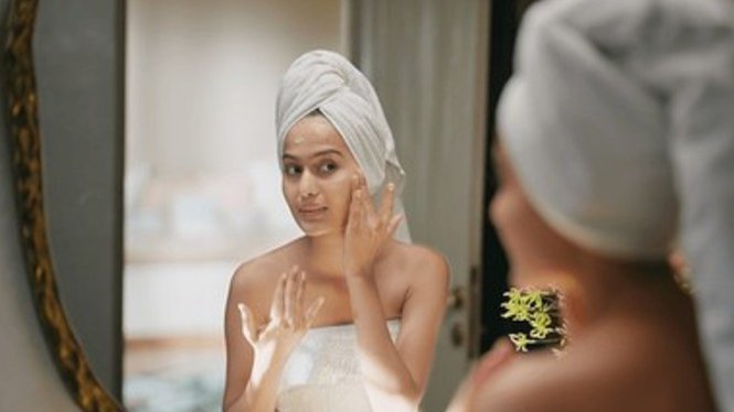 Woman applying night cream to her face while looking in a mirror as part of her nighttime skincare routine