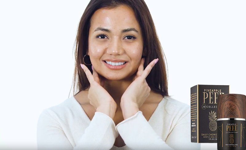 Smiling woman touching her face next to Jo Collection Pineapple Peel daily exfoliator