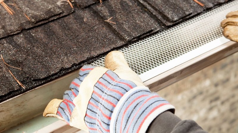 A homeowner inspecting installed gutter guards for accumulated surface debris.