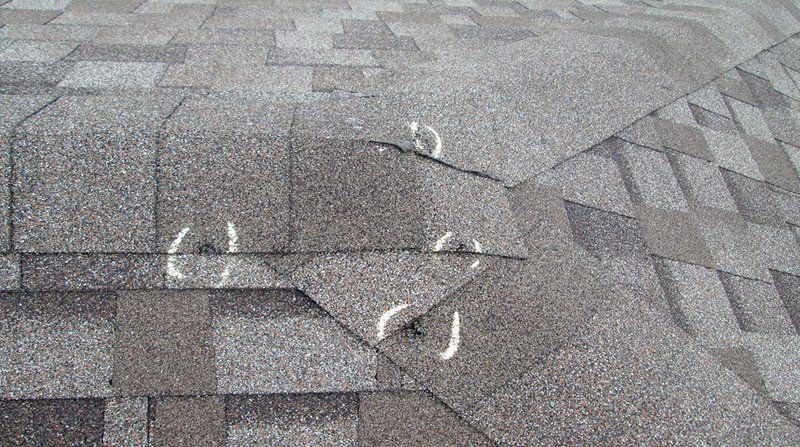 Hail damage roof repair marks circled on cracked asphalt shingles