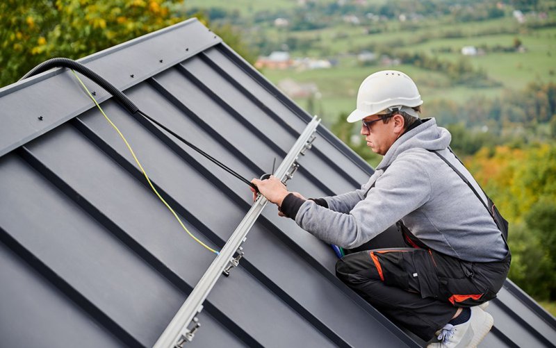 Worker securing standing seam panel during metal roofing installation