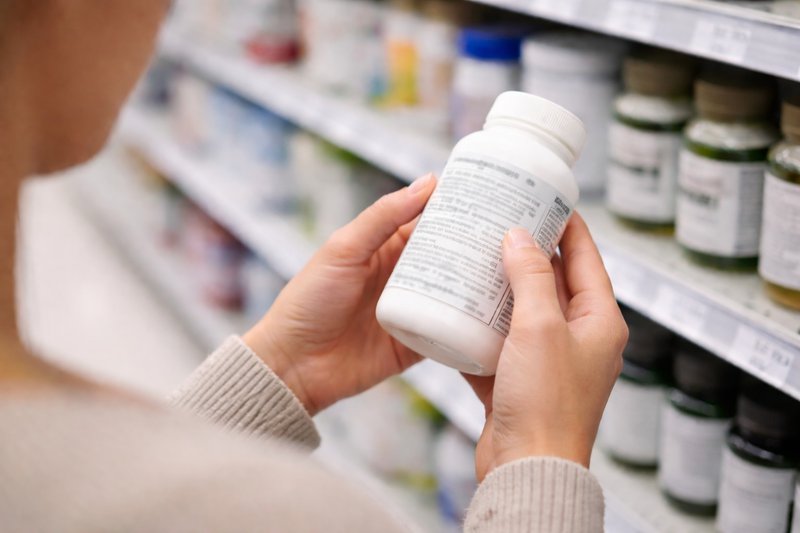 Person examining a supplement bottle label in a store aisle with blurred background shelves