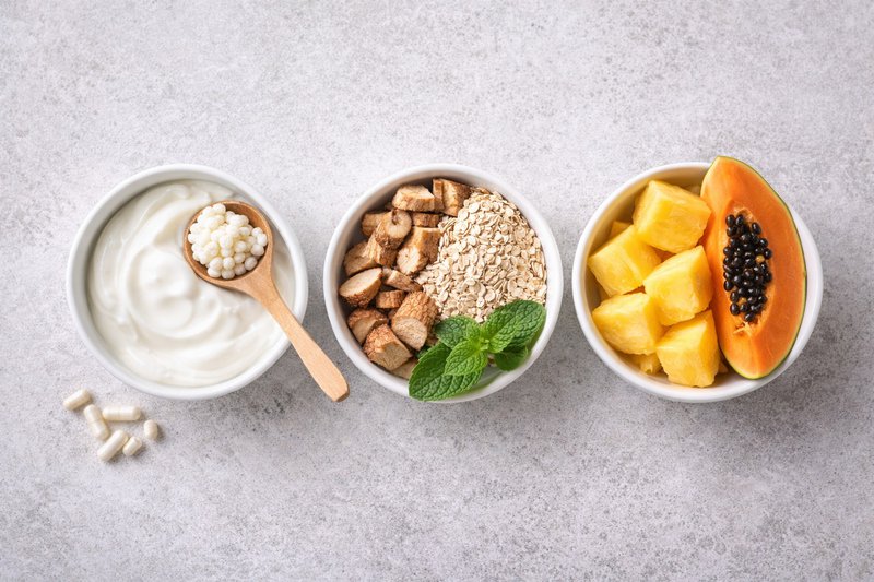 Top-down view of probiotic foods, prebiotic fibers, and enzyme-rich fruits arranged in separate bowls