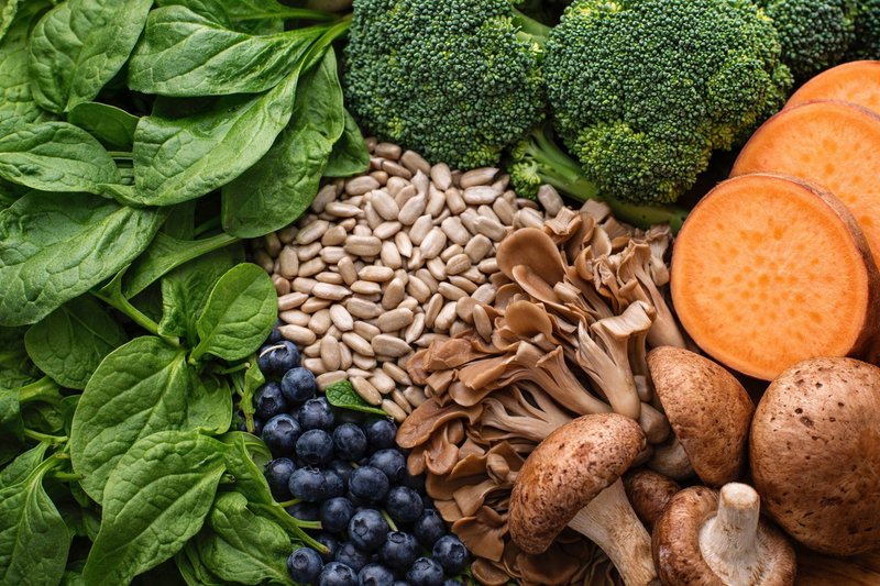 Close-up of spinach, broccoli, mushrooms, sunflower seeds, and sweet potato arranged as natural nutrient sources and supplements for dogs