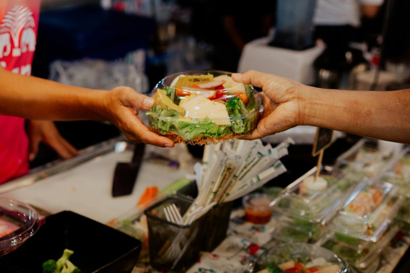 This photo features a bowl of salad being purchased at a market