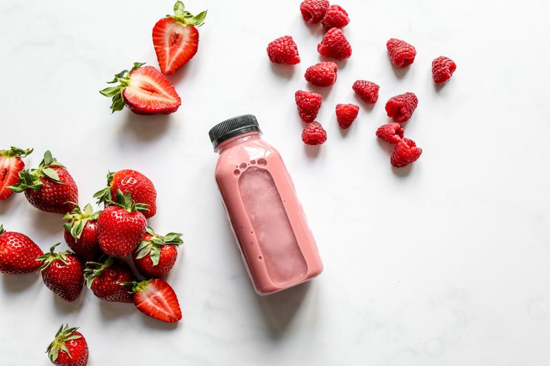 This photo features a bottle of a probiotic drink for gut health surrounded by fresh fruits on a table