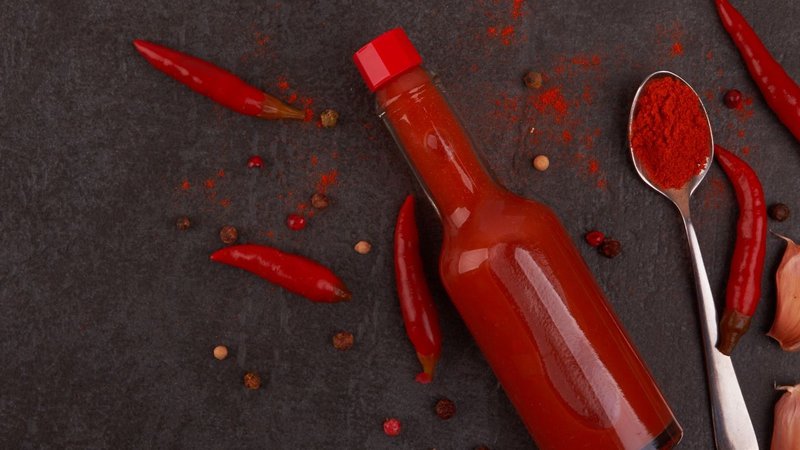 A hot sauce bottle next to fresh spices, showcasing options for glass bottles.
