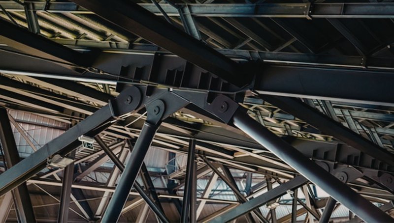 Why HSS Steel Is the Gold Standard for Seismic Resilience 1 A complex network of dark metal beams forming an industrial ceiling made of HSS steel.
