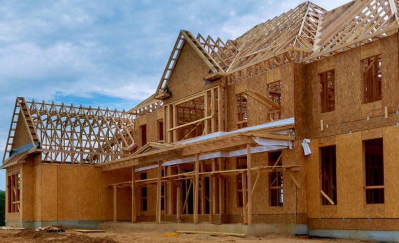 Residential construction site framed with structural beams and roof trusses.