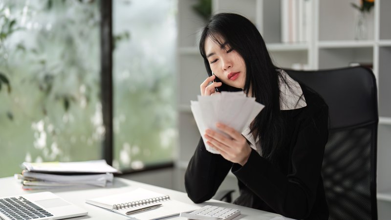Business owner reviewing invoices and financial reports while discussing receivables financing options by phone.