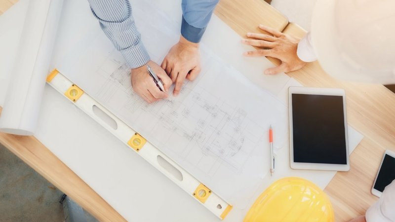 A group in hard hats reviewing blueprints on a table to ensure Built Environment Sustainability.