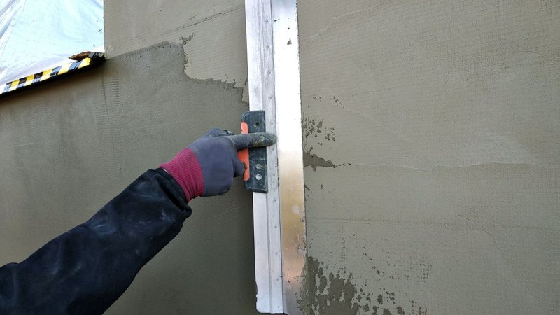 A gloved hand applying stucco to an exterior wall to construct robust Fire Barriers.