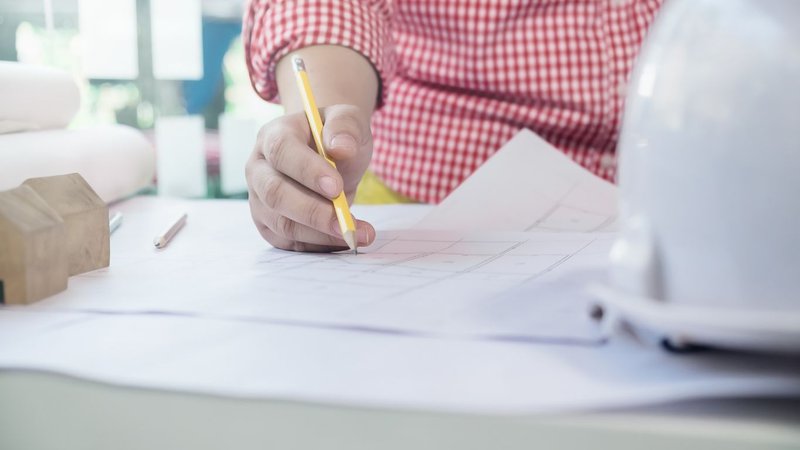 A person reaching over a stack of construction files for Design Development Permitting review.