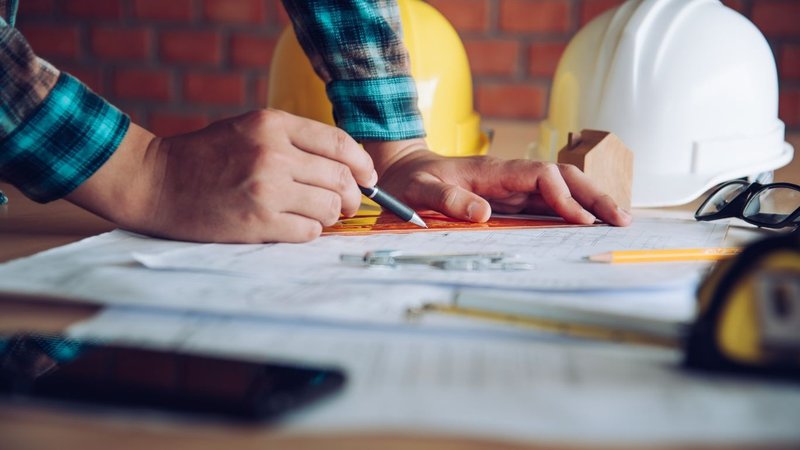 A designer making corrections on blueprints next to a hard hat for Design Development Permitting.