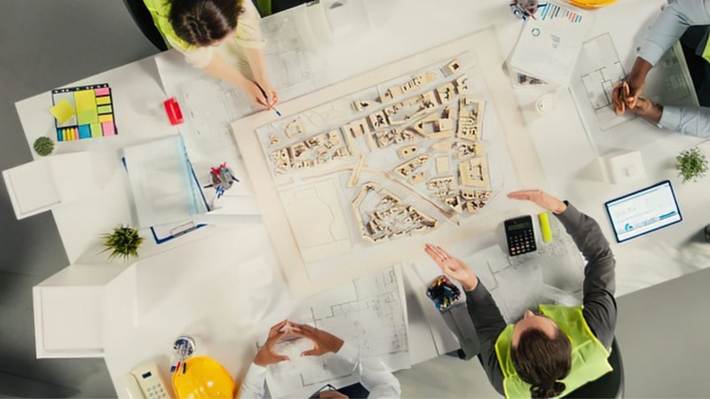 A team collaborating around architectural models and blueprints to review a Zoning Feasibility Study.
