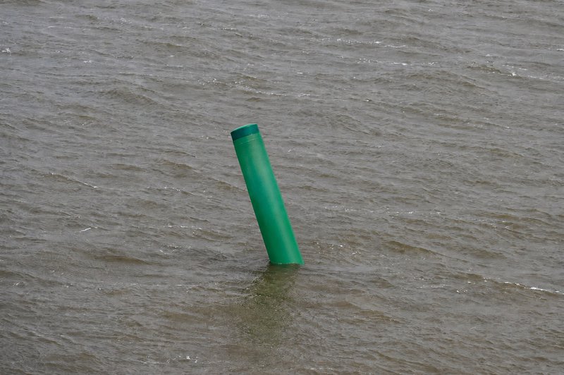 Red numbered channel marker buoy leaning against a piling in murky water