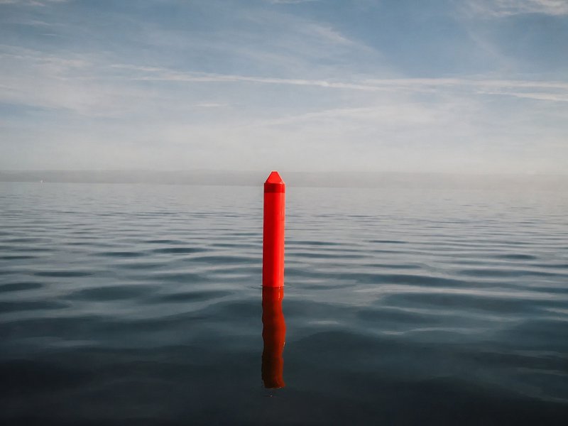 Red lettered buoy marker standing alone on calm open water at dusk  