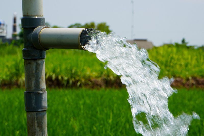 Water pumped from a private well over a green field, showing how PFAS in well water can come from nearby land