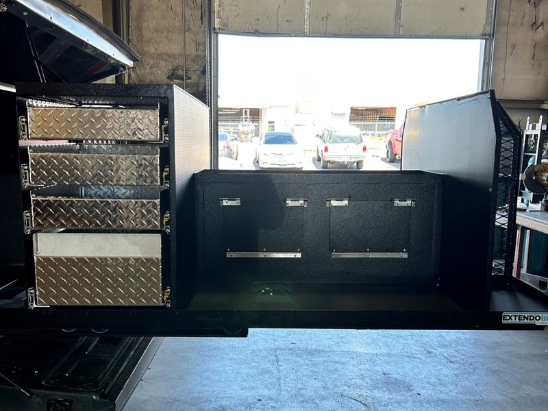 Close-up of truck bed slide out drawers, with diamond-plate drawers open on one side and locking storage compartments on the other.