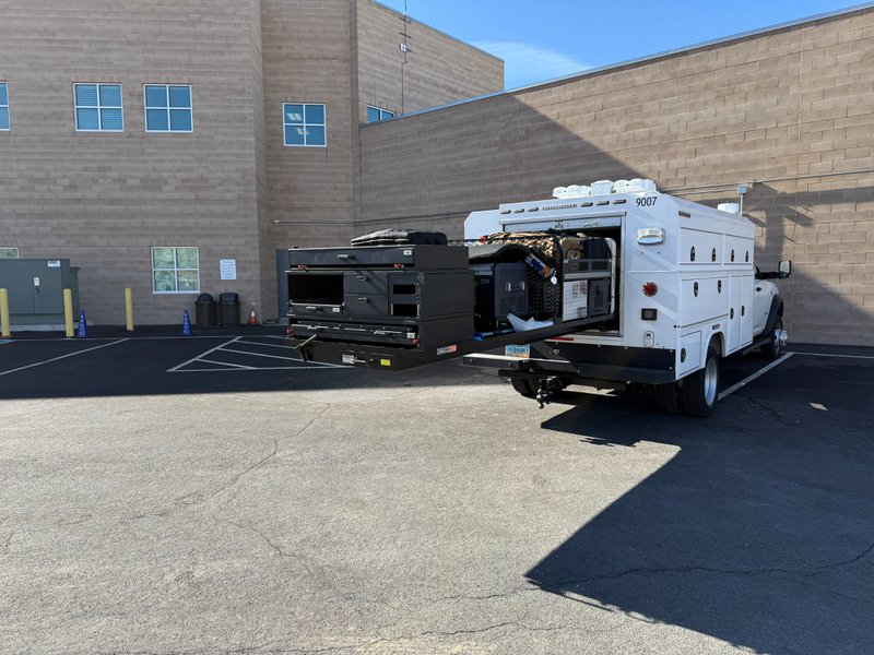 Extendobed slideout tray extended from a service truck with labeled drawers and a portable cooler