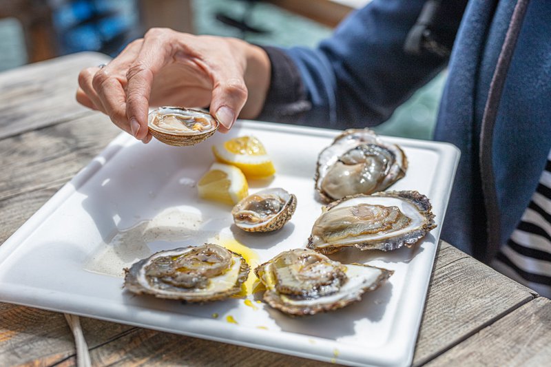 Oesters op een wit bord en persoon neemt er één
