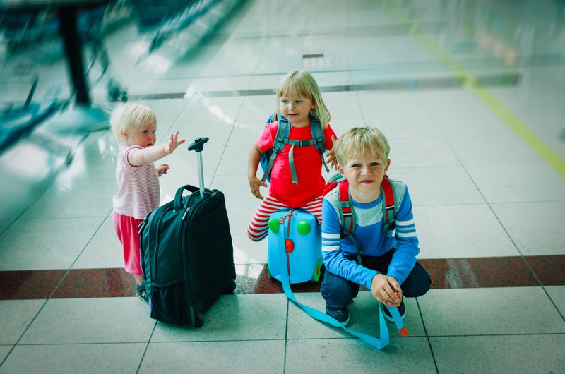 Trois enfants avec leurs bagages à main à l'aéroport.